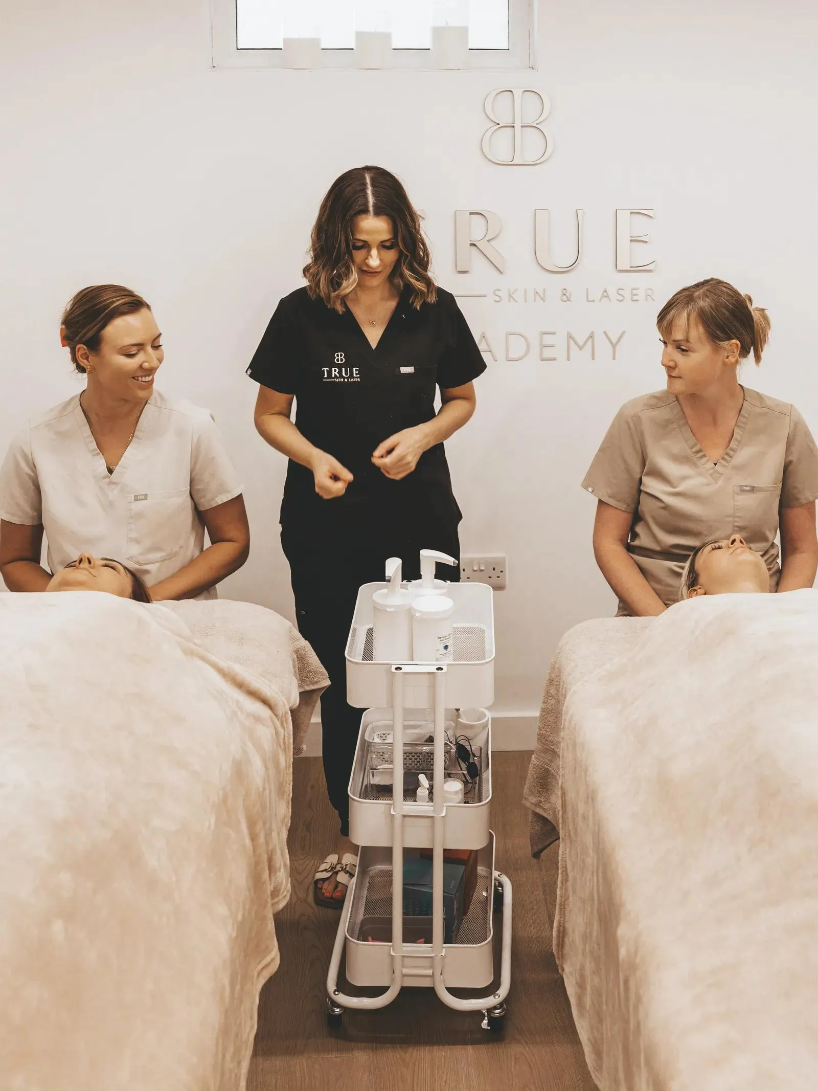 Two trainees each working on a client while Sarah supervises in the academy treatment room