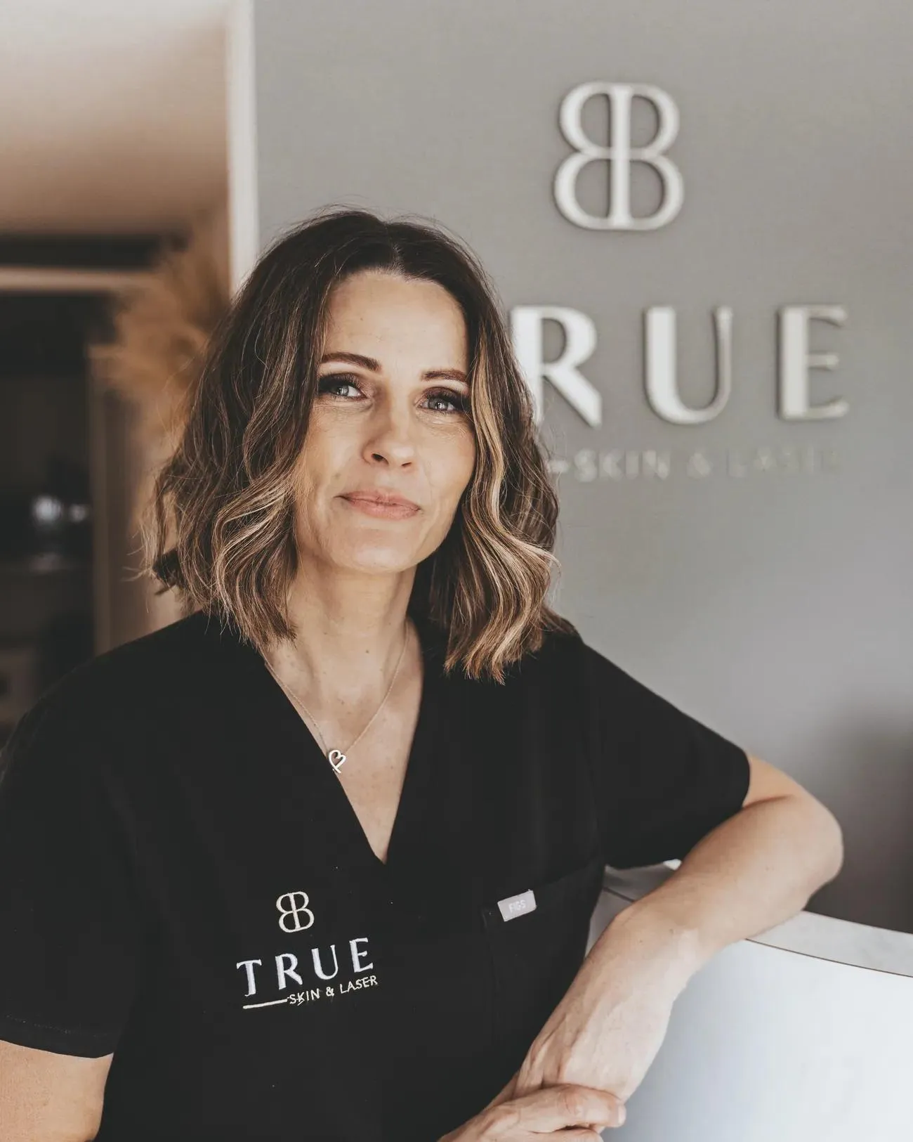 Sarah, founder of True Skin & Laser Academy, in branded black scrubs